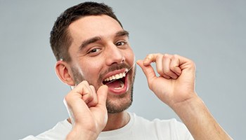 Man flossing to save on the cost of dental emergencies in Barnegat