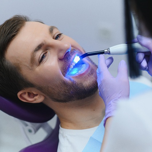 Man in dental chair having tooth-colored filling hardened with UV light