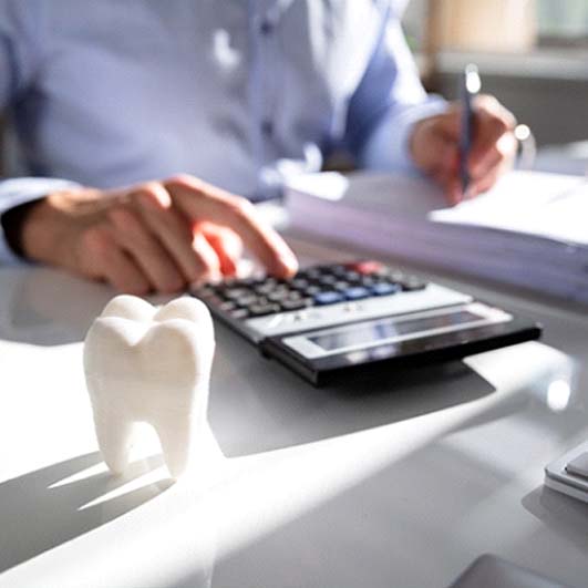 person typing on calculator next to fake tooth