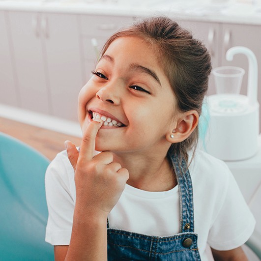 Young girl pointing to her smile during children's dentistry visit