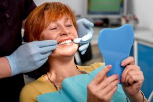Patient admiring implants in mirror in dentist’s chair.